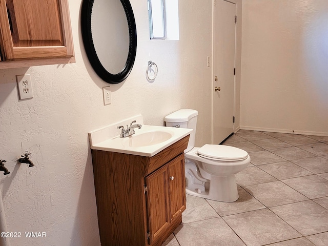 half bath with toilet, tile patterned floors, a textured wall, and vanity