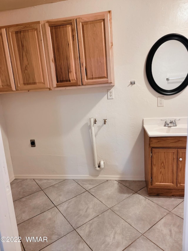 clothes washing area featuring cabinet space, light tile patterned floors, baseboards, and a sink