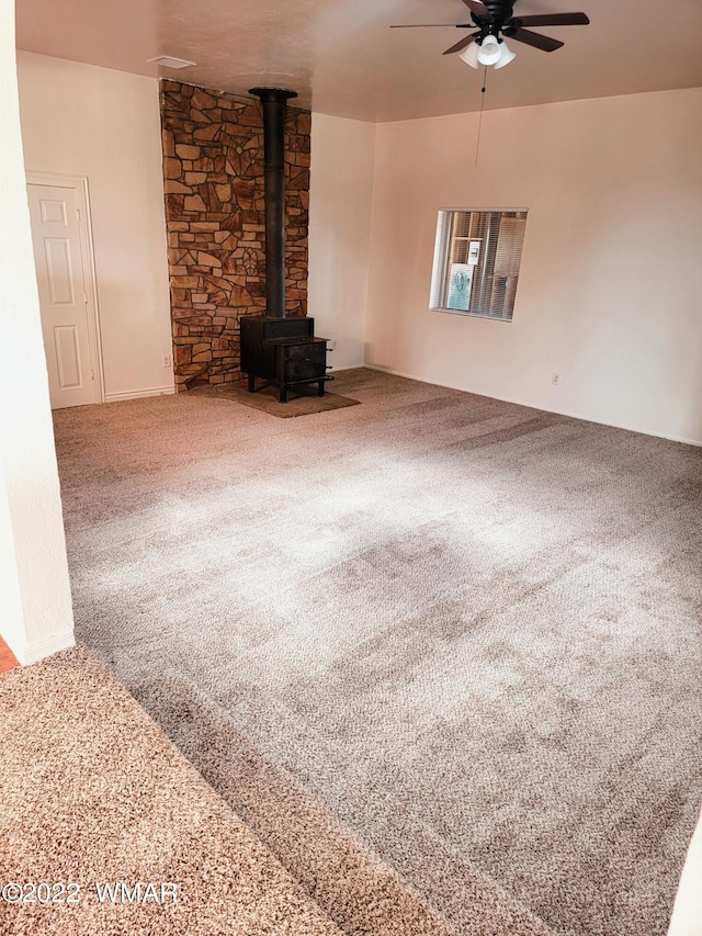 unfurnished living room with carpet floors, a wood stove, and a ceiling fan