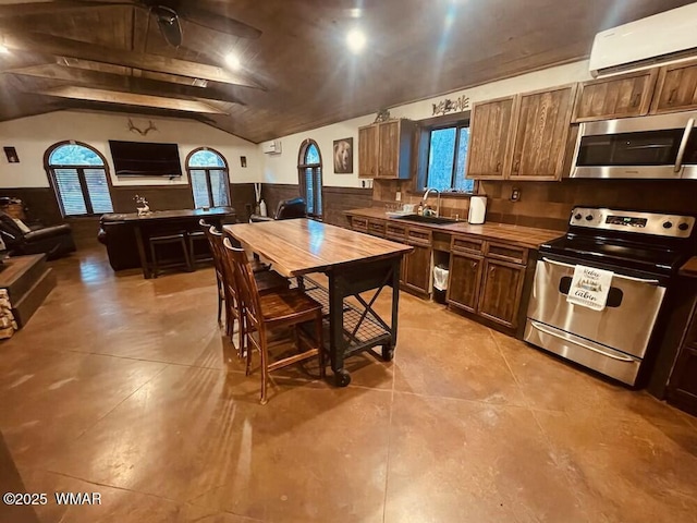 kitchen featuring lofted ceiling, a wall unit AC, a sink, appliances with stainless steel finishes, and wainscoting