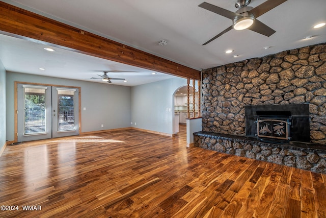 unfurnished living room featuring baseboards, arched walkways, beamed ceiling, wood finished floors, and french doors