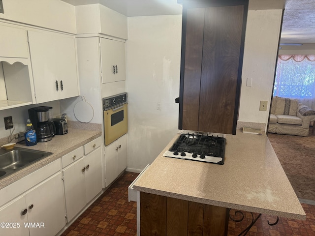 kitchen with oven, light countertops, gas stovetop, white cabinetry, and a sink