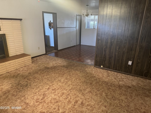 unfurnished living room with a chandelier, dark carpet, and a fireplace