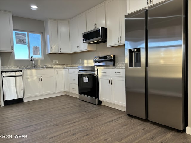 kitchen with light stone counters, a sink, white cabinets, appliances with stainless steel finishes, and dark wood finished floors