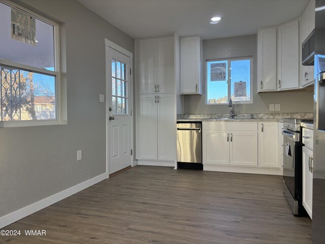 kitchen with appliances with stainless steel finishes, white cabinets, a sink, light stone countertops, and baseboards