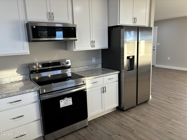 kitchen with light stone counters, stainless steel appliances, white cabinets, wood finished floors, and baseboards