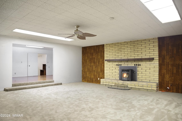 unfurnished living room featuring carpet floors, wood walls, ceiling fan, and a wood stove