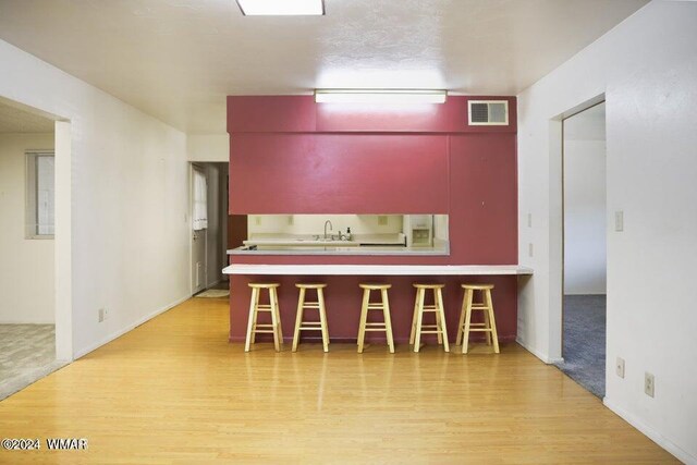 kitchen featuring light wood-style flooring, a peninsula, visible vents, a kitchen breakfast bar, and light countertops