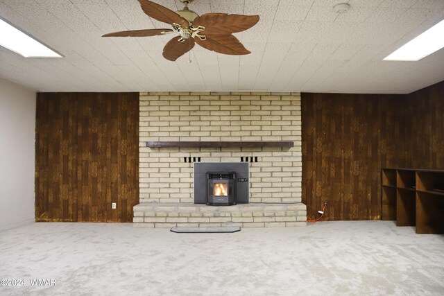 unfurnished living room featuring a ceiling fan, a wood stove, carpet flooring, and wooden walls