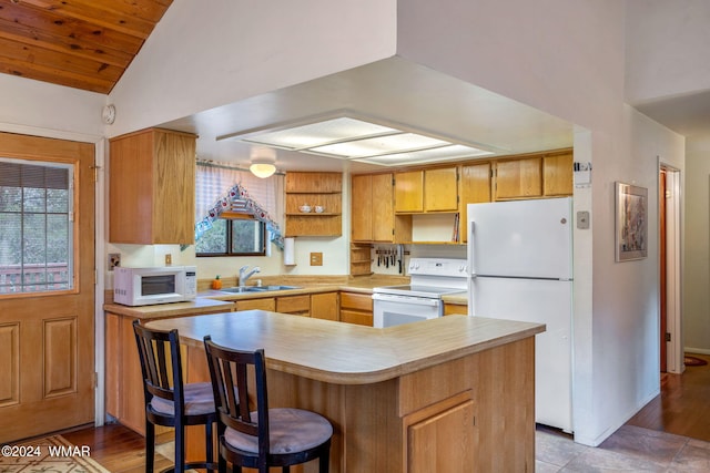 kitchen with light countertops, vaulted ceiling, a sink, white appliances, and a peninsula