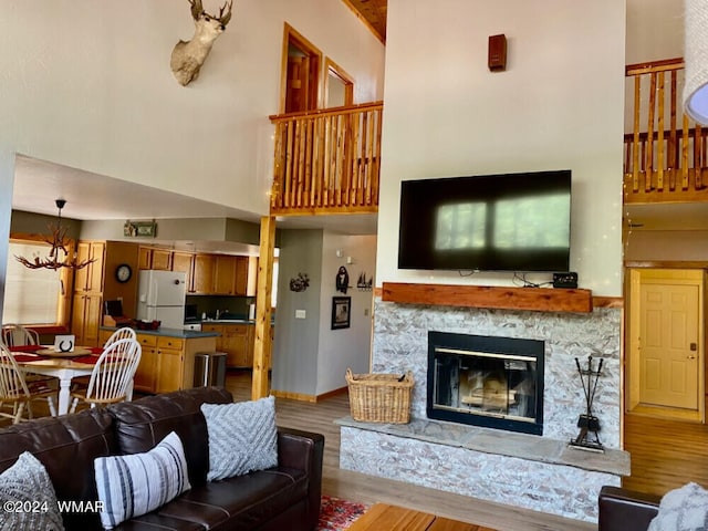 living area with baseboards, light wood-style flooring, a high ceiling, a stone fireplace, and a chandelier