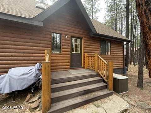property entrance with faux log siding and roof with shingles