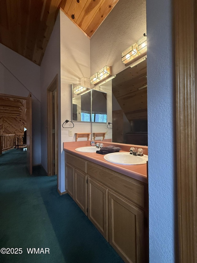 full bathroom with double vanity, a textured wall, vaulted ceiling, and a sink