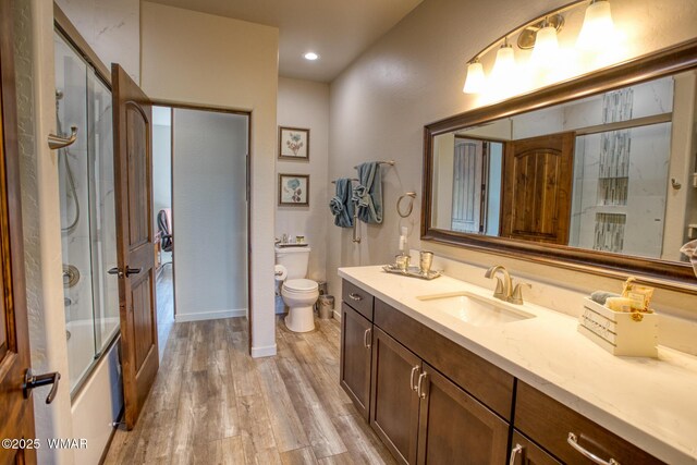 bathroom with toilet, wood finished floors, vanity, combined bath / shower with glass door, and baseboards