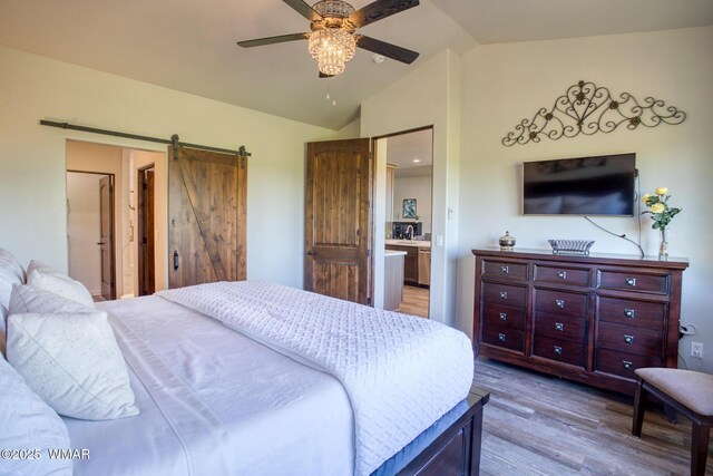 bedroom featuring vaulted ceiling, ceiling fan, a barn door, and wood finished floors