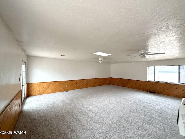 carpeted empty room featuring wainscoting, a skylight, and wooden walls