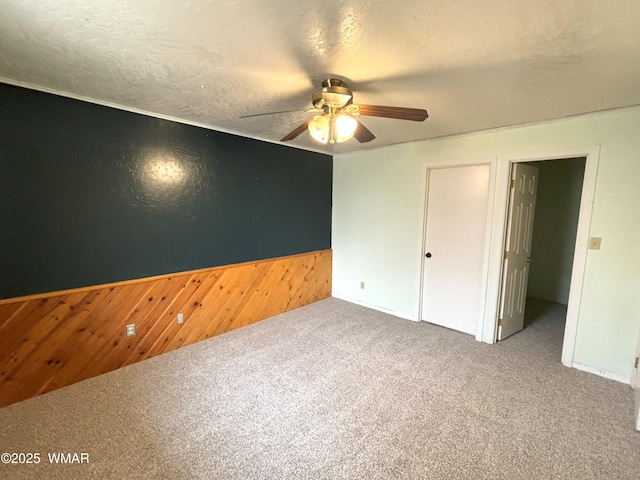 unfurnished bedroom with a ceiling fan, wainscoting, carpet flooring, wooden walls, and a textured ceiling