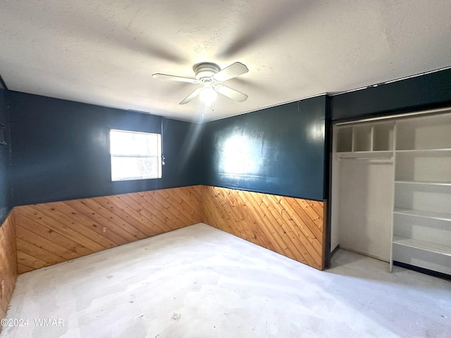 unfurnished room with a wainscoted wall, ceiling fan, wood walls, and a textured ceiling