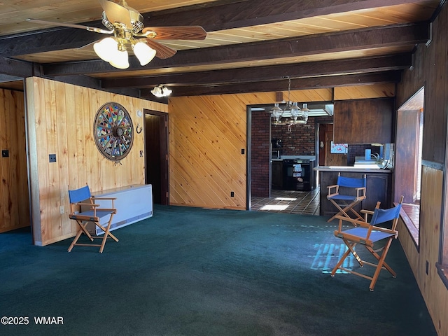 interior space with ceiling fan with notable chandelier, dark colored carpet, wood walls, and beam ceiling