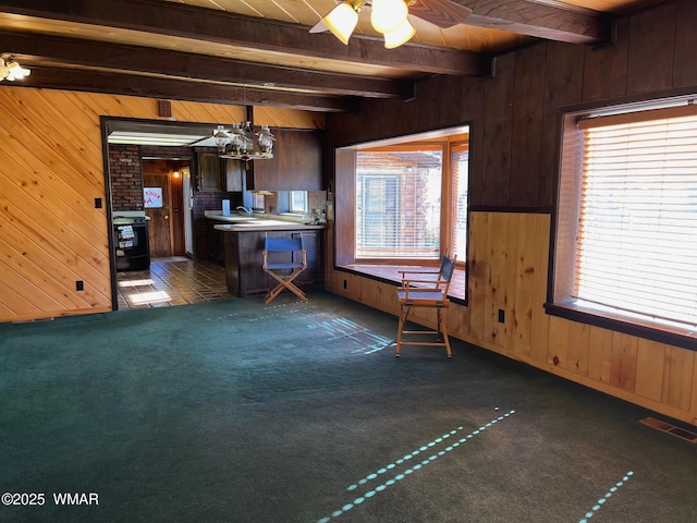 interior space with visible vents, beamed ceiling, dark colored carpet, dark brown cabinets, and wood walls