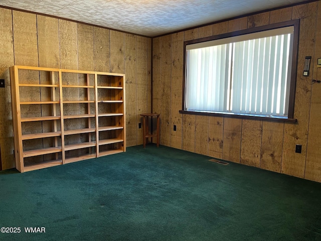 empty room featuring dark colored carpet, visible vents, and wood walls