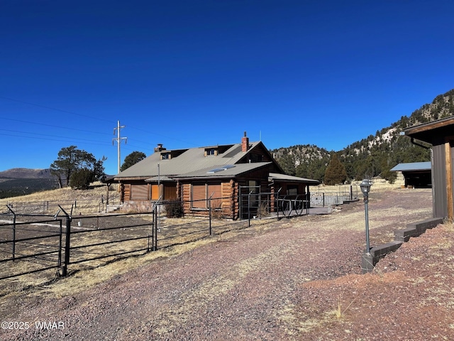 view of front of home featuring log siding, a rural view, an outdoor structure, a mountain view, and an exterior structure