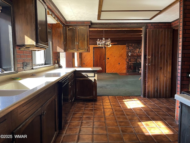 kitchen featuring dark brown cabinetry, black dishwasher, light countertops, wood walls, and a sink