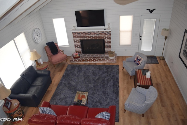 living room featuring a brick fireplace, vaulted ceiling, and wood finished floors