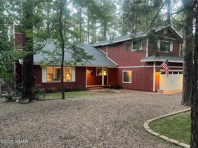 view of front of home featuring roof with shingles, an attached garage, and gravel driveway