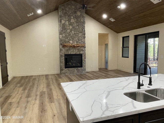 kitchen featuring wood ceiling, open floor plan, light stone countertops, a stone fireplace, and a sink