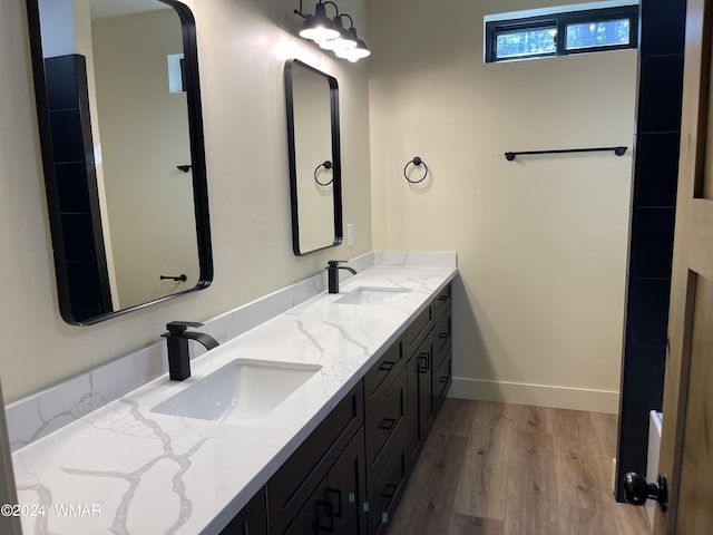 bathroom with double vanity, baseboards, a sink, and wood finished floors