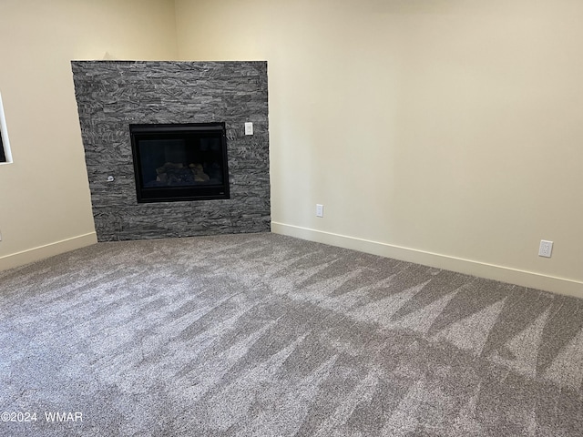 unfurnished living room with a stone fireplace, carpet flooring, and baseboards