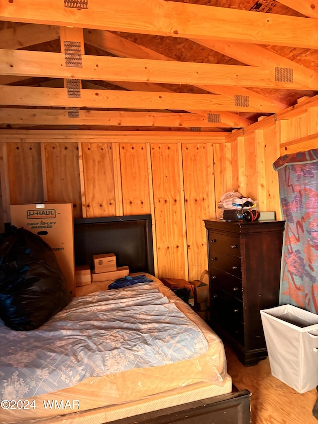 bedroom featuring vaulted ceiling with beams, wood walls, and light wood-style floors