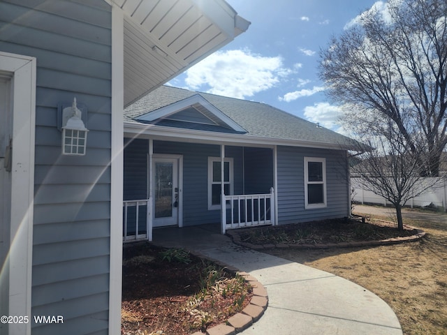 doorway to property with covered porch and roof with shingles