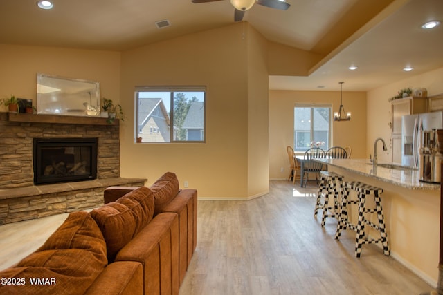 living area with light wood-style flooring, recessed lighting, a stone fireplace, baseboards, and vaulted ceiling