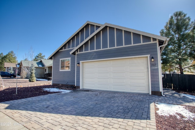 view of front of house featuring decorative driveway, fence, board and batten siding, and an attached garage