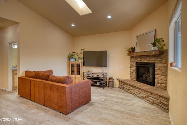 living area with baseboards, light wood-type flooring, recessed lighting, vaulted ceiling with skylight, and a fireplace