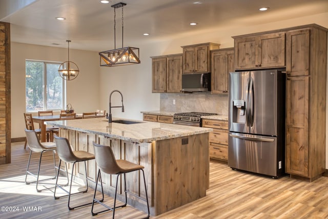 kitchen featuring light stone counters, a sink, appliances with stainless steel finishes, an island with sink, and pendant lighting