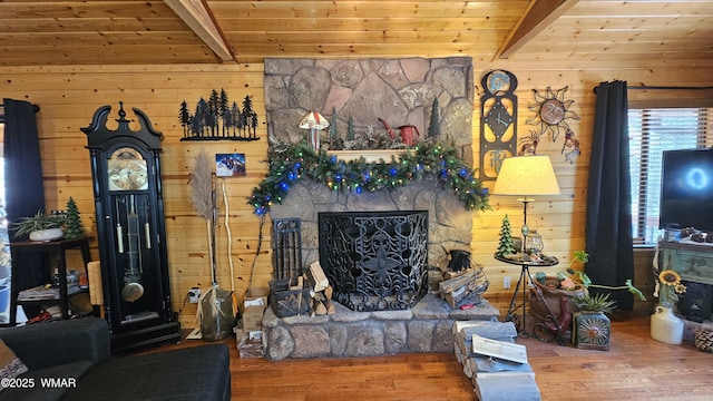 living area featuring a stone fireplace, beam ceiling, and wood finished floors