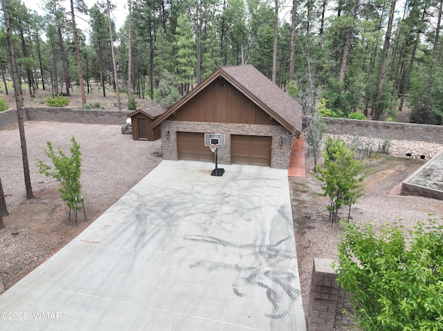 exterior space featuring a garage, driveway, stone siding, and a wooded view