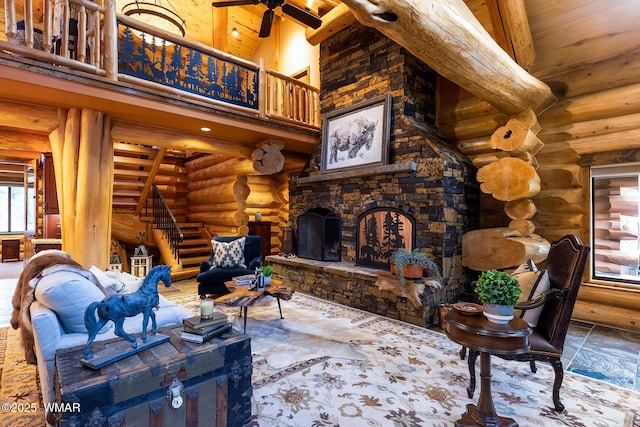 living area with log walls, a high ceiling, stairs, wood ceiling, and a stone fireplace