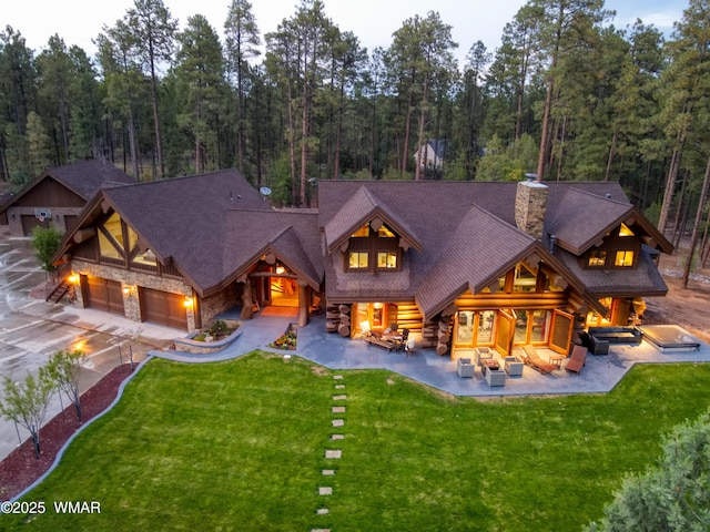 back of property featuring a wooded view, a lawn, and an outdoor living space with a fire pit