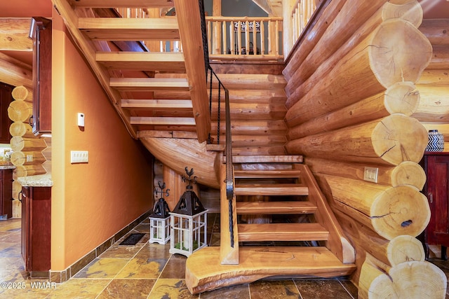 staircase featuring rustic walls, stone tile flooring, and baseboards