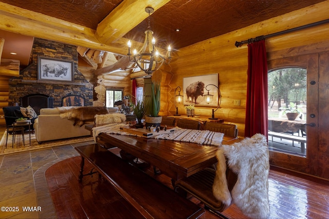 dining room featuring an inviting chandelier, a fireplace, wood-type flooring, log walls, and beam ceiling