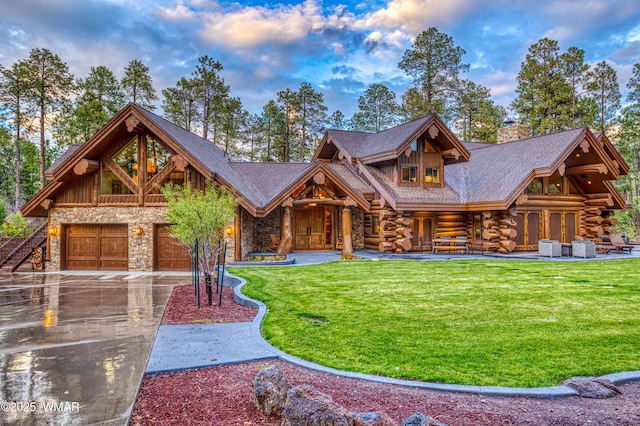 log-style house with a chimney, concrete driveway, a front yard, log siding, and stone siding