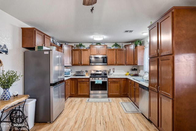 kitchen with brown cabinetry, light wood-style floors, stainless steel appliances, and light countertops