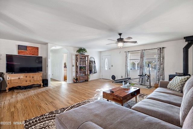 living room featuring a ceiling fan, arched walkways, a wood stove, and light wood-style flooring