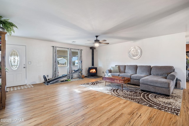 living room featuring a wood stove, ceiling fan, and wood finished floors