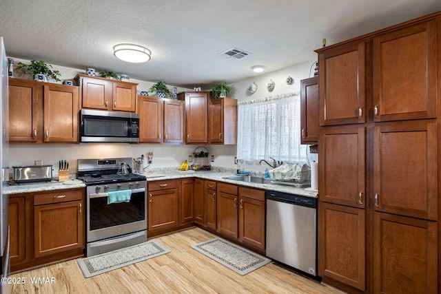 kitchen with brown cabinets, light wood-style flooring, visible vents, and stainless steel appliances