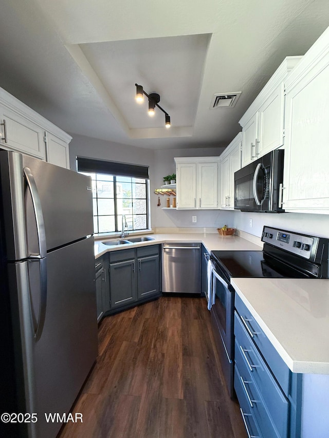 kitchen featuring white cabinets, appliances with stainless steel finishes, light countertops, and a tray ceiling